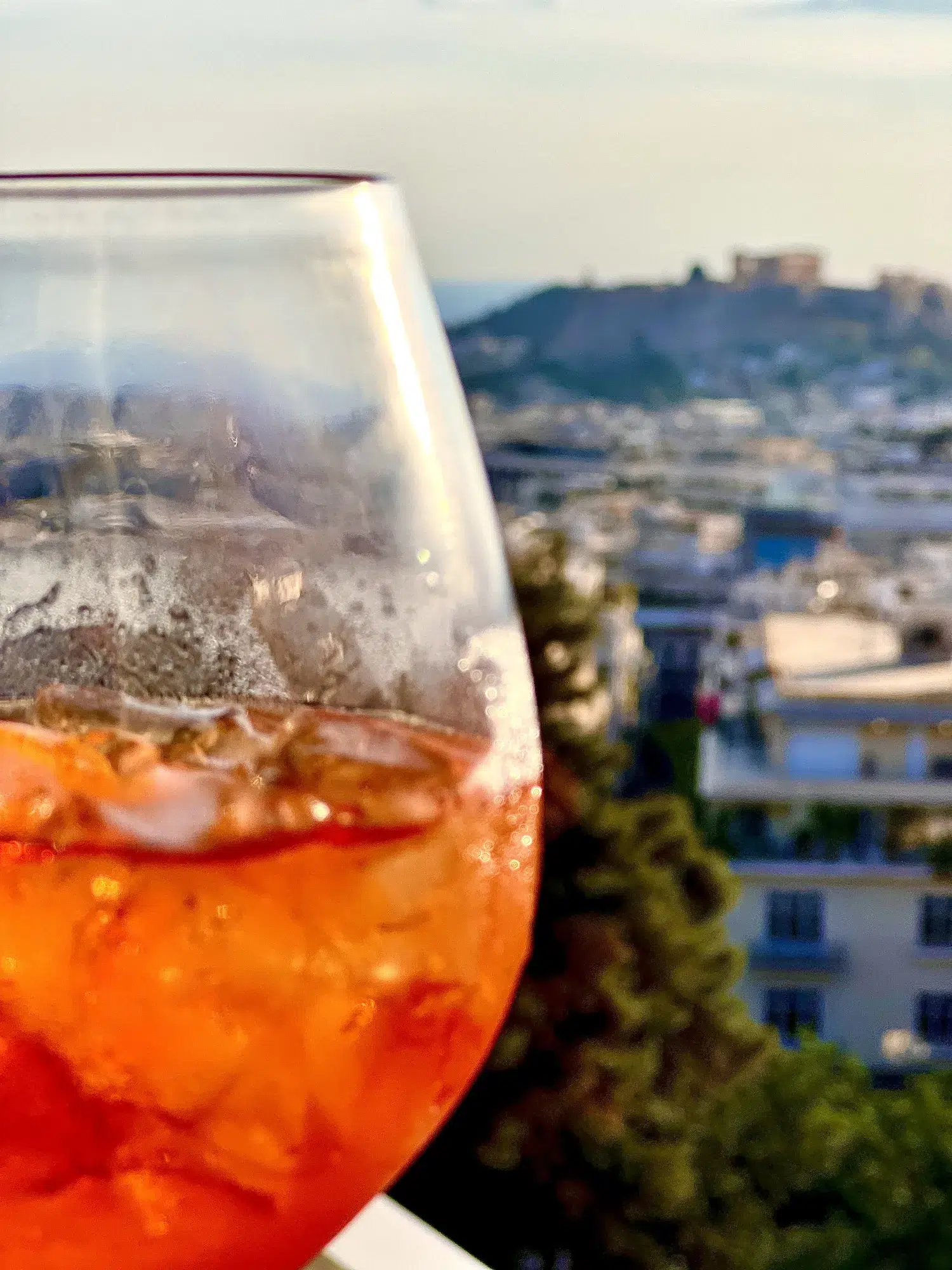 Ein Glas mit orangefarbenem Getränk und Eis vor einer sonnigen Stadtansicht